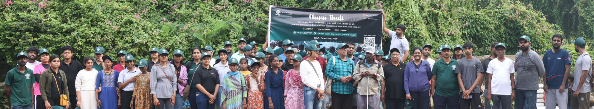 Large diverse group of volunteers wearing matching teal caps and colored clothing standing together outdoors in front of a green banner with Meiporul branding, smiling and united in their commitment to community service and social impact